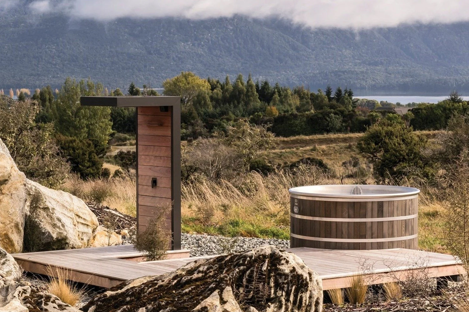 Round stainless steel spa pool with cedar cladding and outdoor shower on timber deck overlooking New Zealand landscape